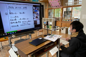 電子黒板に教員用ＰＣ画面とＷｅｂカメラで投影した教員を提示。書画カメラと指向性マイクも使っている